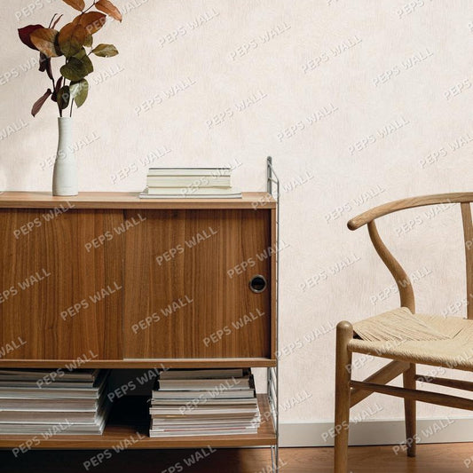 Beige textured wallpaper shown in a styled interior scene with a wooden cabinet, books, a vase with dried leaves, and part of a wooden chair.