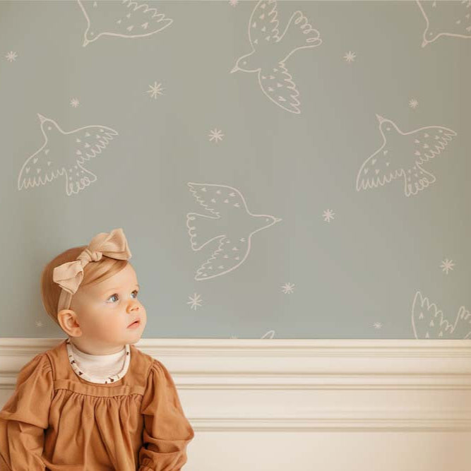 Wallpaper Kids Nursery Dubai Peps Wall A young child sitting in front of a wall with blue wallpaper featuring whimsical bird patterns.