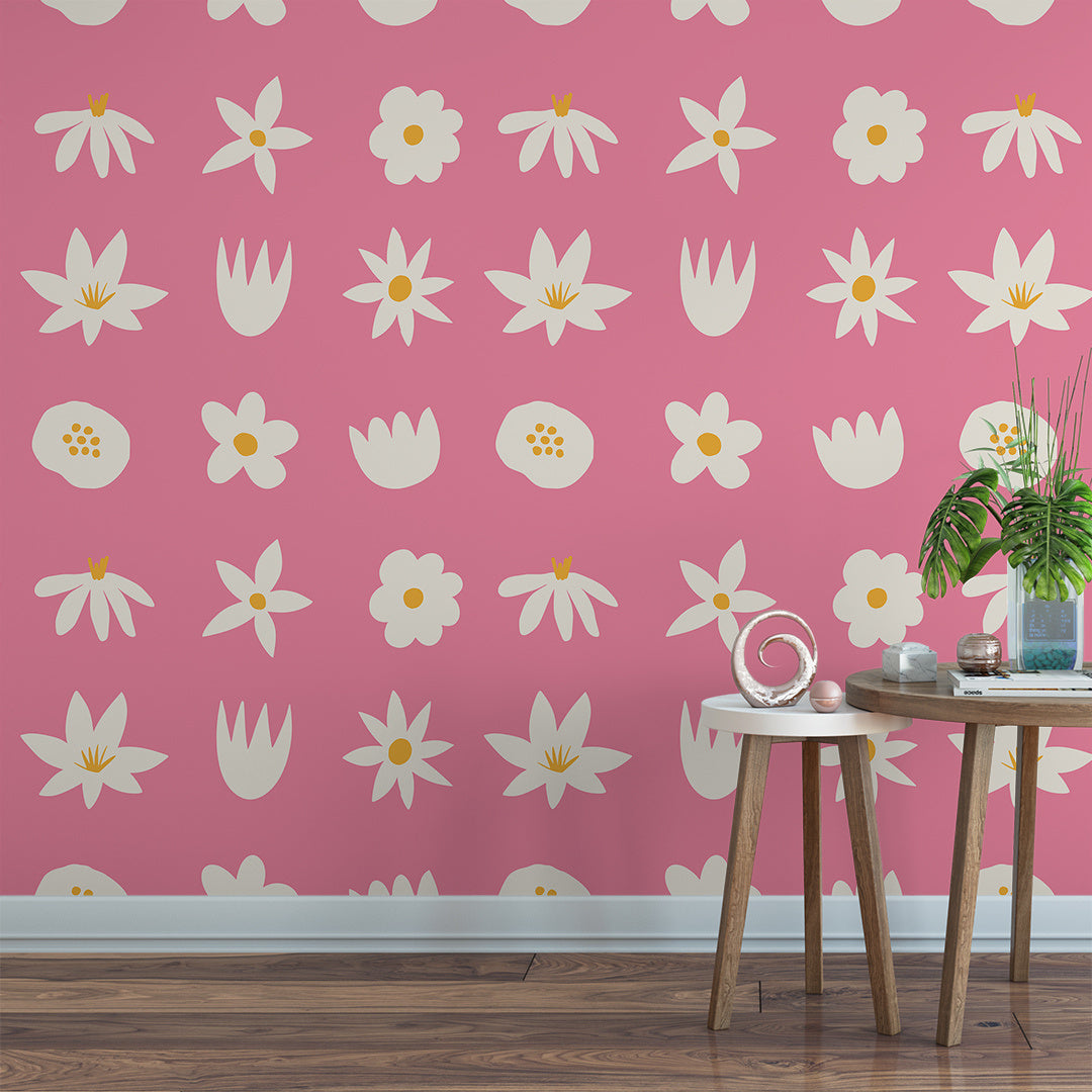 Wallpaper Kids Nursery Dubai A room with pink wallpaper featuring a repeating pattern of white flowers with yellow centers. A wooden side table and a chair are placed in the room, and a green plant is seated on the table.