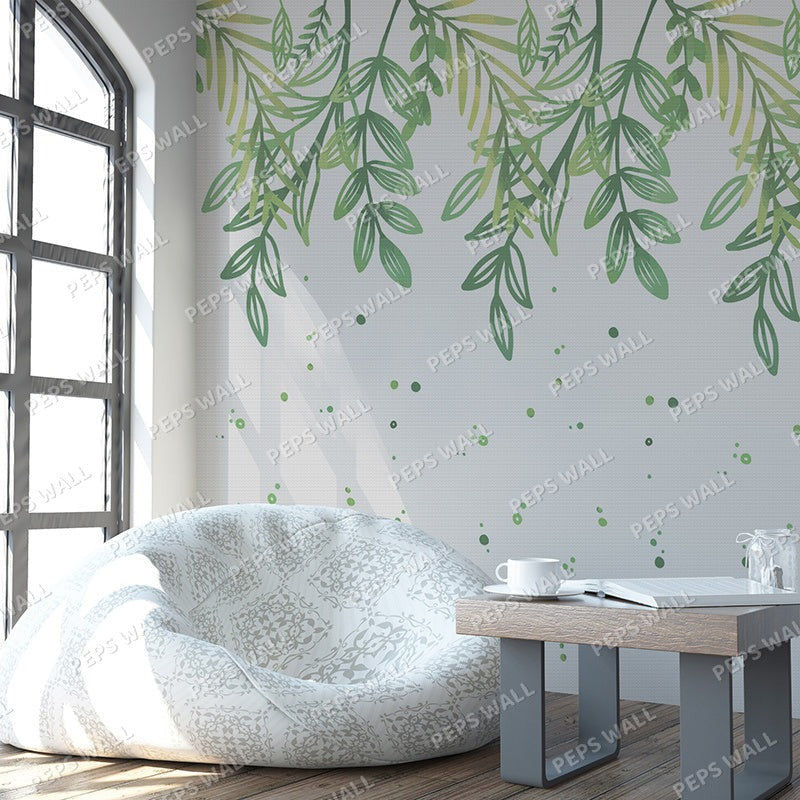 Wallpaper Kids Nursery Dubai A room with a wall decorated with green leaf patterns, featuring a beanbag chair and a small wooden table with a white mug and a book.