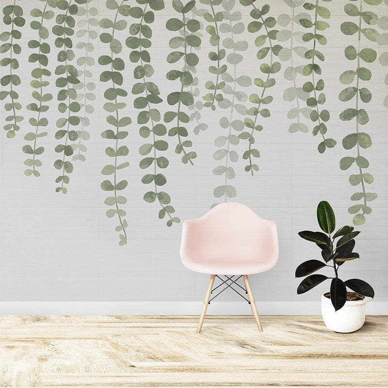 Wallpaper Kids Nursery Dubai A wall adorned with a mural of green leaves in various shades, hanging downwards, creating a botanical and serene ambiance. A pink chair and a potted plant are positioned in the room, complementing the greenery theme.