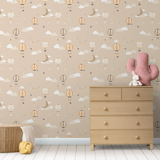 Wallpaper Kids Nursery Dubai Peps Wall A room with wallpaper featuring various cartoonish designs including balloons, clouds, and cacti, with a wooden dresser and a pink cactus toy in the foreground.
