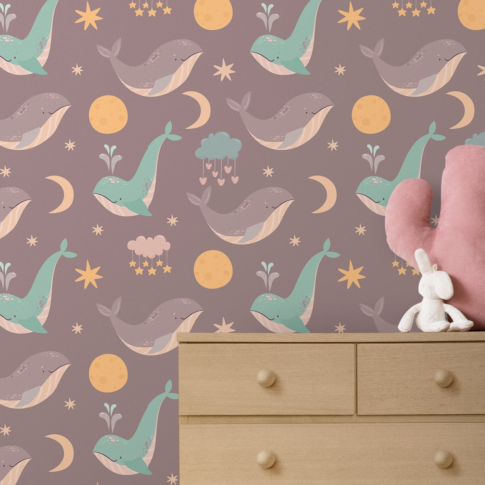 Wallpaper Kids Nursery Dubai Peps Wall A wallpaper with a pattern of colorful whales, stars, and moon on a purple background, displayed in a room with a pink toy whale and a white toy rabbit.