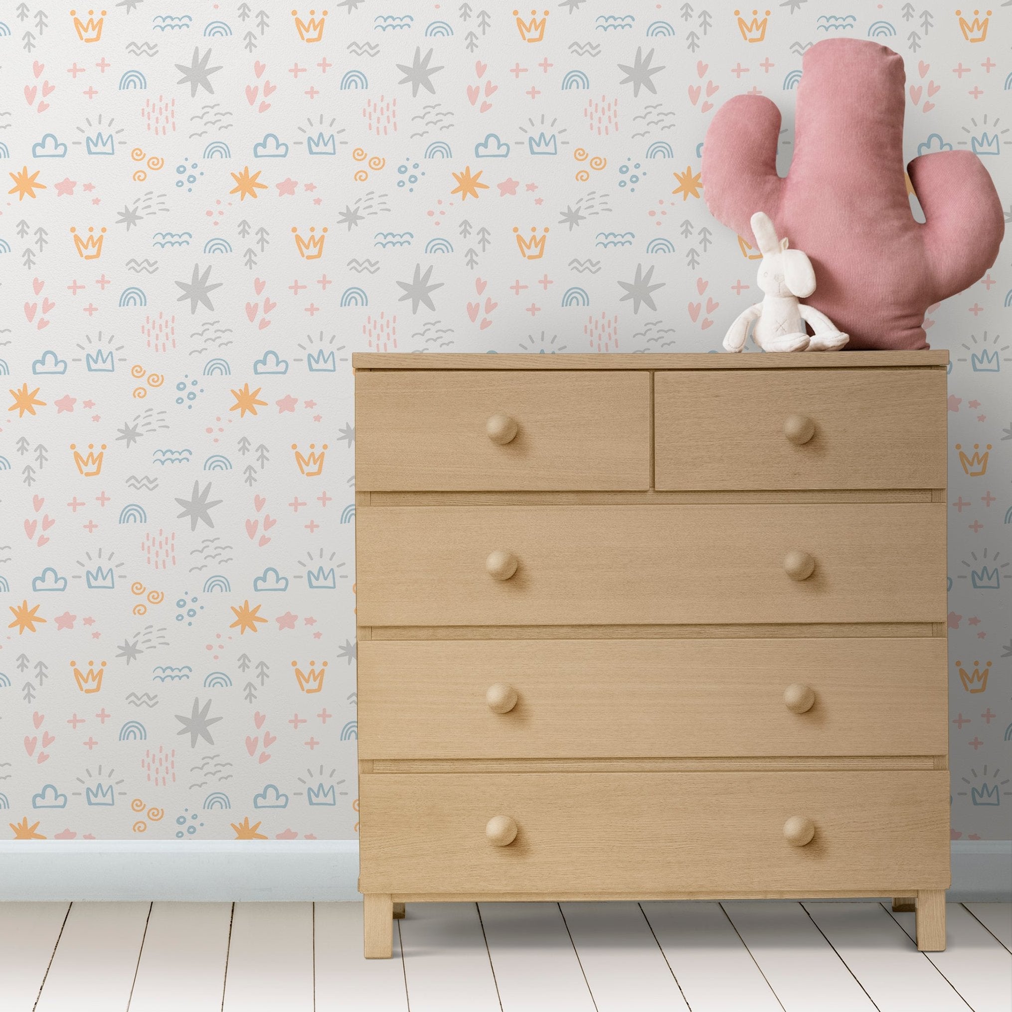A wall with a graffiti-style pattern featuring cacti, stars, and other abstract designs in a colorful palette against a white background. A beige wooden dresser with four drawers is positioned against this wall, with a pink toy cactus on top.