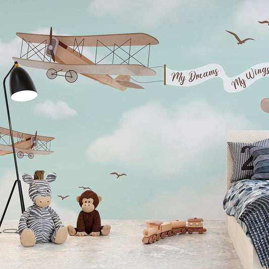 Wallpaper Kids Nursery Dubai Peps Wall A wall decal featuring a vintage airplane with a banner reading 'My Dreams My Wings', surrounded by rainbows and clouds, applied on a wall alongside soft toys and a wooden train set.