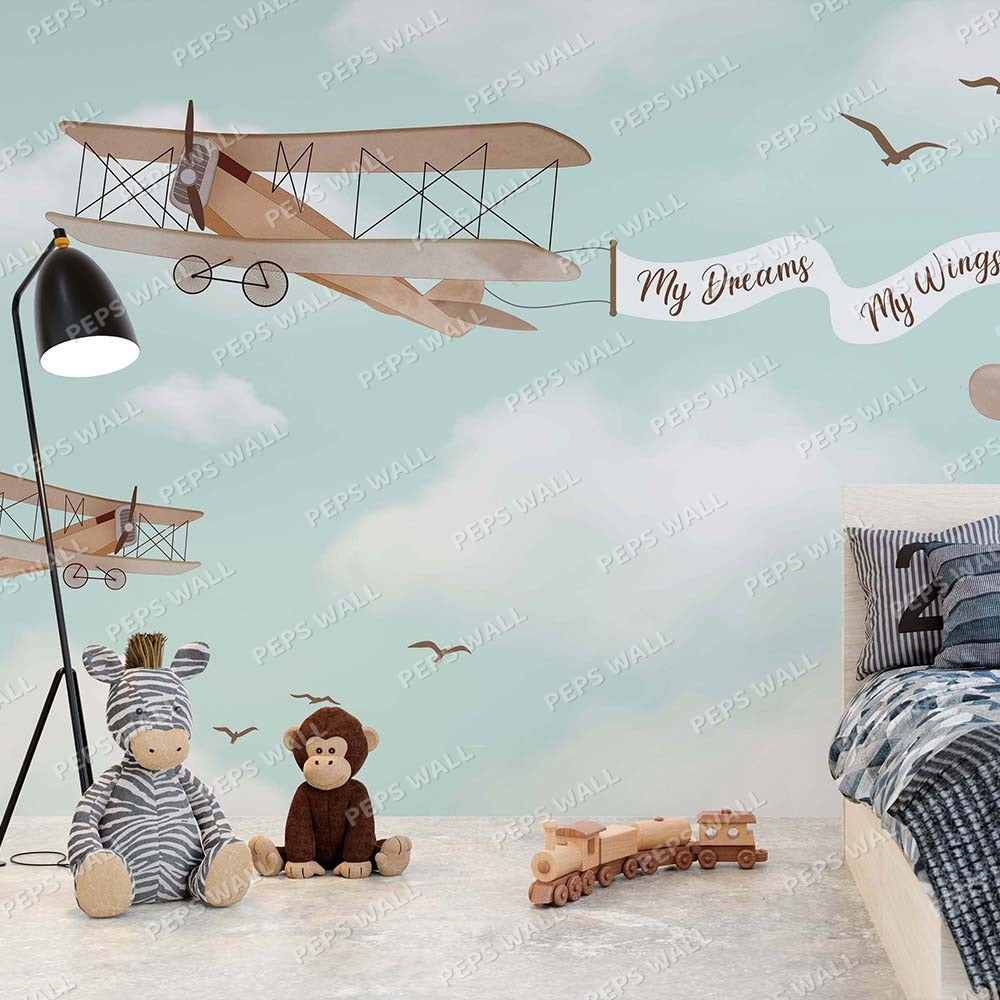 Wallpaper Kids Nursery Dubai Peps Wall A wall decal featuring a vintage airplane with a banner reading 'My Dreams My Wings', surrounded by rainbows and clouds, applied on a wall alongside soft toys and a wooden train set.