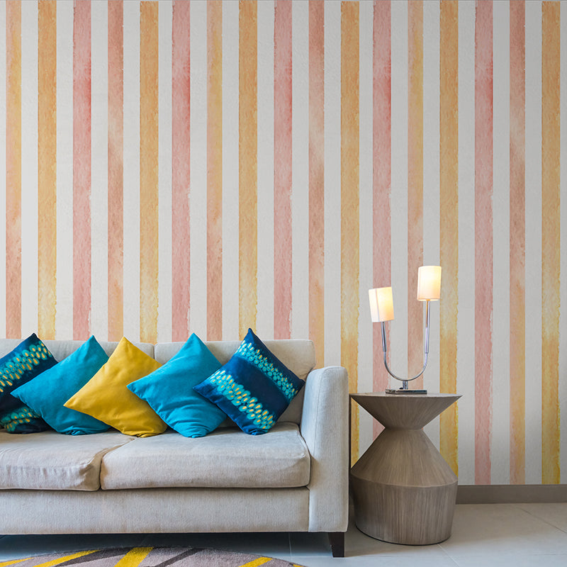 Wallpaper Kids Nursery Dubai Peps Wall A living room with a colorful striped wall decor featuring abstract and graffiti-style patterns in multiple colors, with a beige sofa, blue and yellow pillows, and a wooden side table with a lamp.