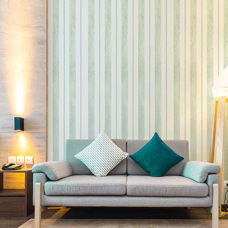 Wallpaper Kids Nursery Dubai Peps Wall A living room with green stripes on the wall, featuring a sofa with cushions, a side table with a lamp and a phone, and a wood floor.