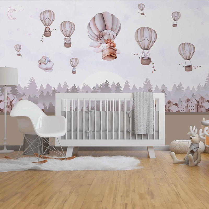 Wallpaper Kids Nursery Dubai Peps Wall A nursery room with wall decor featuring hot air balloon patterns and a mountain range in the background. A white crib is placed in the room, and there is a white chair and a decorative animal figure to the side.